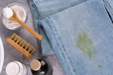 Dirty jeans with grass on their knees are ready for home stain removal. Cleaning supplies such as a brush, sponge, and jars of powder. The concept of eco-friendly stain removal on clothes. top view