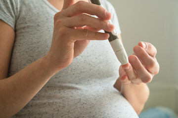 Future mother performing important glucose test during pregnancy. Close-up of finger prick blood sampling for diabetes screening and prevention.