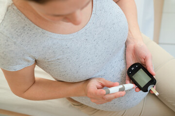 Expectant mother checking her blood glucose with a meter. A personal and important moment in managing gestational diabetes during pregnancy. Close-up, top view.