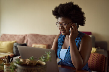Young African woman talking on a phone and working on a laptop