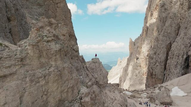 Wide establishing of Toni Demetz Hut between Sassolungo peaks in South Tyrol, Dolomites, Italy, pullback from man on cliff edge
