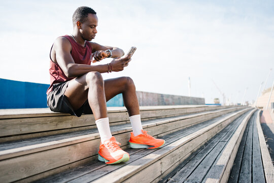 Young African American man checking cardio fitness levels on smartwatch and using mobile phone app to do sport