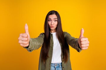 Cheerful young woman in casual fashion giving enthusiastic thumbs up on a vibrant yellow background