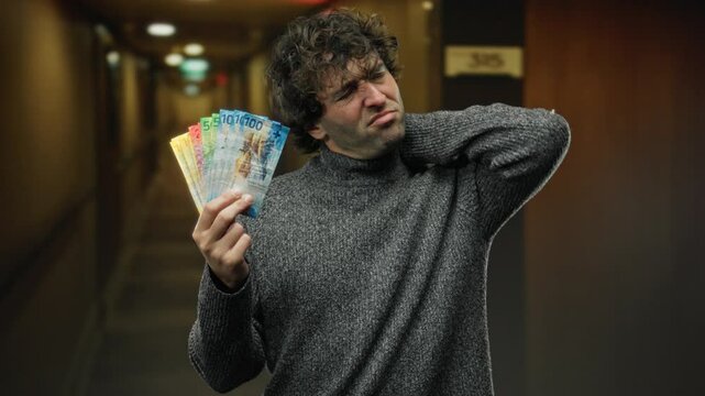 Man holding swiss francs at hotel reception with a pained expression indicating discomfort in his neck indoors.