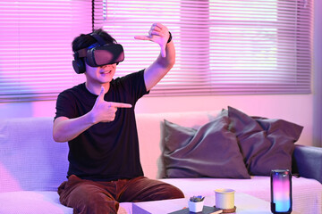 Man sitting on apartment living room couch wearing augmented reality glasses moving his hands while...