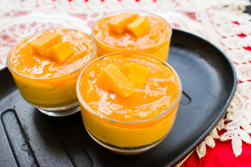 Homemade Mango Cheesecake in Glass Jars on Rustic Black Tray. summer recipes, food styling, elegant...