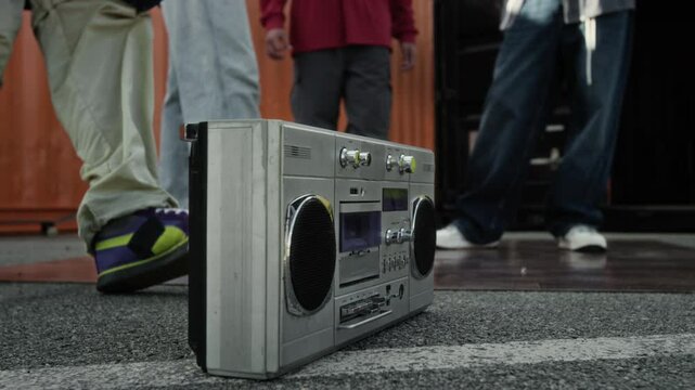 Ground level cropped shot of unrecognizable cool guy in hip hop outfit putting cassette into silver old school boombox on ground then joining group of friends enjoying music together