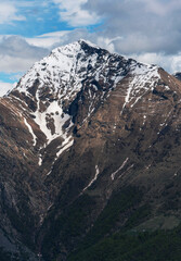 Striking vertical close-up of Monte Legnone's summit, highlighting its sharp, rocky ridges, lingering snowfields, and the intense blue sky of the Italian Alps. Orobie range