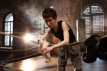 A woman in a boxing gym, portrait by the ropes, cinematic style, dark tones. Training and overcoming oneself, motivation