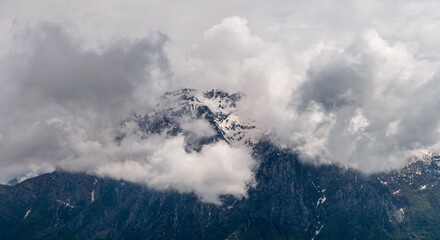 Majestic panorama of Grigna Settentrionale (Grignone) and Pizzo della Pieve, their imposing rocky summits partially veiled by swirling clouds, creating a mysterious alpine atmosphere. Lombardy