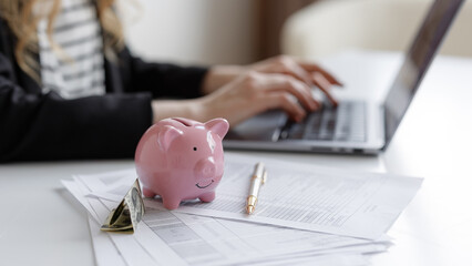 Managing personal finances with a laptop, piggy bank, and documents at a desk during daylight hours