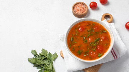 Vegetable fresh soup with tomatoes and herbs in white bowl on linen napkin. Copy space