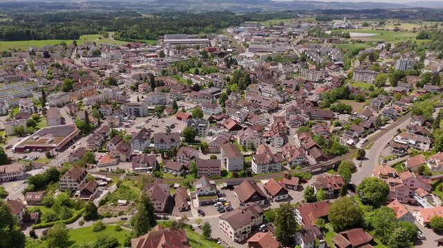 Swiss Buildings and houses of Hinwil in Summer season. Aerial top down shot. Red tile roofs of houses in idyllic small swiss district. Green forest trees in distance.