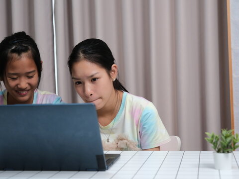 Two girls are sitting at a table looking at a laptop - Powered by Adobe