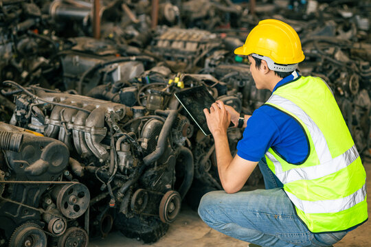 technician male worker working in scrapyard finding used car engine block order from customer at storage recycle area in warehouse