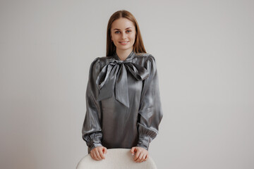 Model poses in stylish gray blouse against minimalistic backdrop during indoor fashion shoot