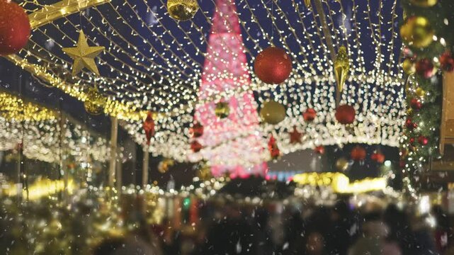 People walk around the city in the evening during Christmas, the first snow falls. Holiday lights illuminate bustling market square with festive decorations. Winter city