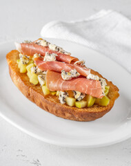 Toasted sandwich with blue cheese, prosciutto, sautéed apple, honey, white plate