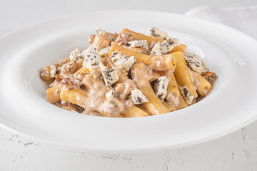 Penne pasta served with creamy walnut blue cheese sauce on white plate