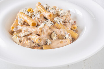 Penne pasta served with creamy walnut blue cheese sauce on white plate