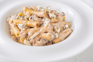 Penne pasta served with creamy walnut blue cheese sauce on white plate