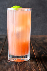 Guava Collins cocktail sparkles in tall glass with lime against dark backdrop