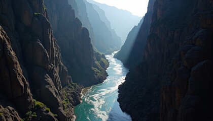 Turquoise river winds through a deep canyon with sunrays piercing through the hazy mountain air.