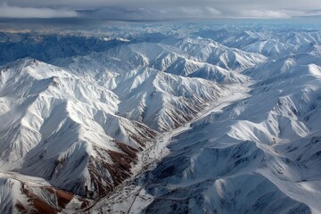 Obraz premium Majestic snow-capped mountains overlook a winding river under a cloudy sky in a remote location