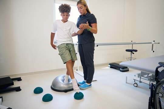 Physiotherapist assists patient in standing balance activity using balance discs