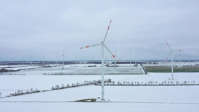 Windpark am Stadtrand mit hoher Anzahl an Windkraftanlagen im Winter von der Luft aus gesehen