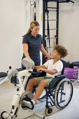 Boy uses an arm bike under the guidance of therapist