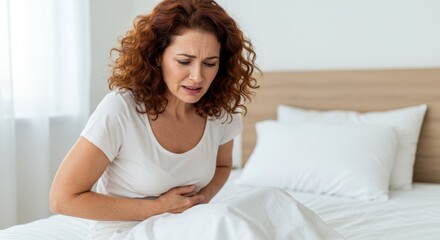 Naklejka premium Woman clutching stomach in pain sitting on bed