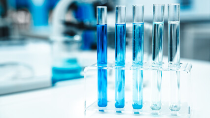 Test tubes filled with blue liquid arranged in a metal rack next to a microscope, representing scientific research, chemical analysis, and biotechnology in a modern laboratory setting.