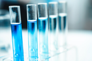 Test tubes filled with blue liquid arranged in a metal rack next to a microscope, representing scientific research, chemical analysis, and biotechnology in a modern laboratory setting.