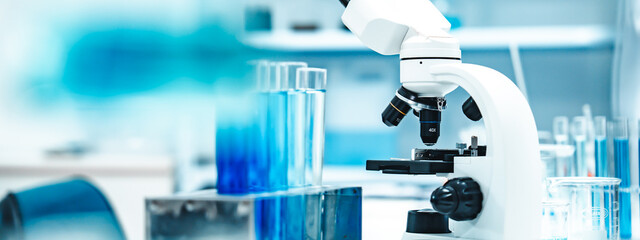 Test tubes with blue liquid in a stainless rack beside a white microscope in a clean laboratory,...