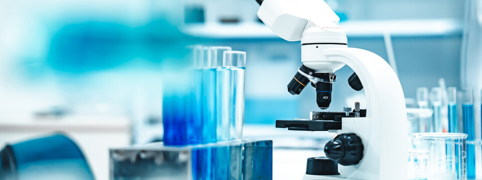 Test tubes with blue liquid in a stainless rack beside a white microscope in a clean laboratory, representing scientific research, analysis, and modern biotechnology processes.