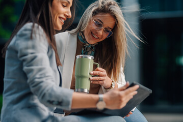 Businesswomen using tablet and drinking coffee outdoors