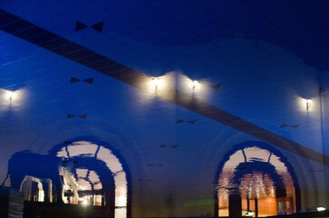 Dimly lit hotel corridor showcases arched reflections on pool water surface, with ambient yellow...