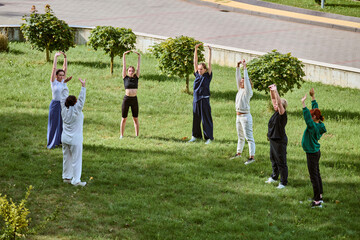 Adults of various ethnicities practicing qigong outdoors, bending forward in grassy park. Bright...