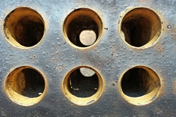 Detailed view of six circular holes in a weathered metallic surface on a sunny day