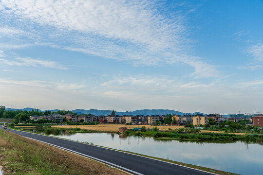 Residential houses along a riverbank under a blue sky with clouds.