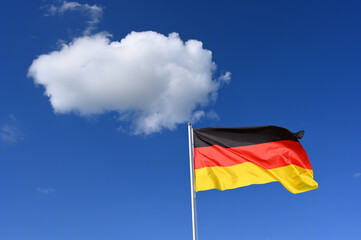 The flag of  Germany flutters in the wind in a blue sky with white cloud