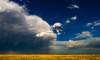 Low-angle light shines through storm clouds over colorful fields, creating a dramatic sky with rich...