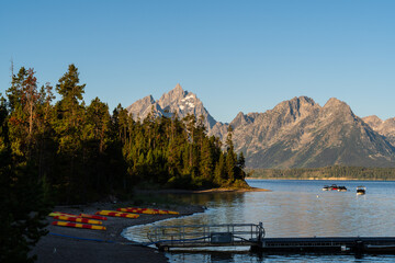 Sunrise over a beautiful mountain lake and forests fills the sky with color and soft clouds, creating a tranquil, scenic view of nature, wilderness, and the peaceful start of a new day.
