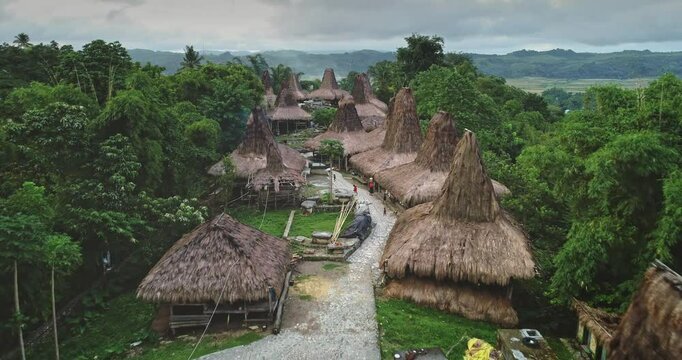 Aerial view of unique custom houses with high, thatched roofs forming a captivating ancient village in a remote area of Sumba island, Indonesia, with local people walking on a path