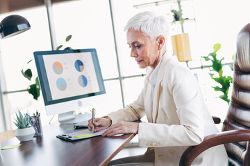 Senior businesswoman working diligently in her office, analyzing data and handling documents,...