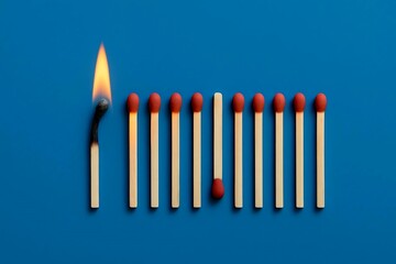 Close-up of a lit burning matchstick surrounded by unlit matches on vibrant blue background