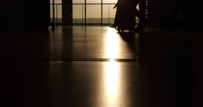 Airport floor, brightly reflects evening sun, legs and wheeled suitcases of passengers passing through departure zone moving forth and back. Scene is high contrast, showcasing bustling travel routine