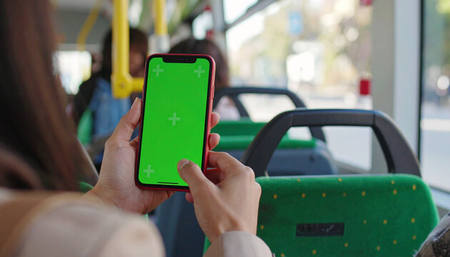 Woman holding smartphone with green screen mockup on public bus, editable phone display

