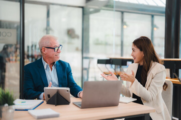 Obraz premium Senior businessman and young businesswoman discussing strategy during a meeting in a modern office, using laptop and tablet, collaborating on a project and sharing ideas